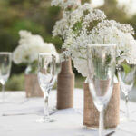 A table set with wine glasses and vases of flowers.