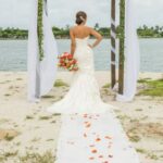 A bride standing on the beach in front of an arch.