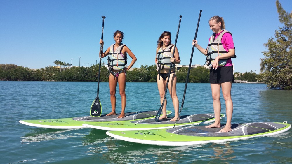 Three women are standing on paddle boards in the water.